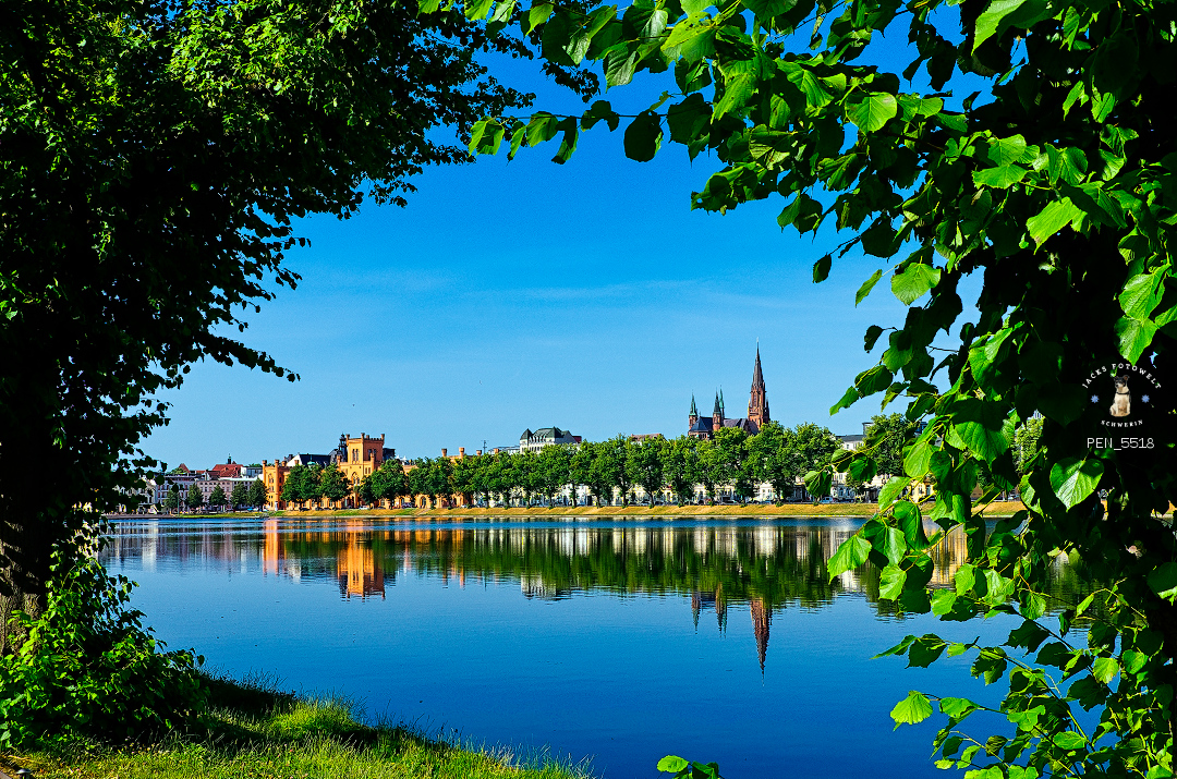 Eingerahmt - der Pfaffenteich – Mitten in der Stadt Schwerin liegt der Pfaffenteich. Ein einst künstlich angelegtes Gewässer zum Flanieren und verweilen.  Hier zeigt sich der Pfaffenteich, der mit dem Aubach und dem Ziegelinnensee verbunden ist, mit einer leichten Umrahmung aus natürlichem Grün. Der Pfaffenteich ist auch im Schwerin Kalender zu finden, den ihr auf https://fotowelt-schwerin.de erwerben könnt.